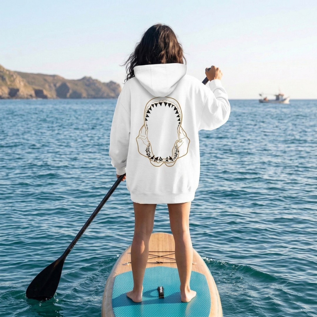 Person on a stand-up paddleboard wearing a hoodie with a shark design.